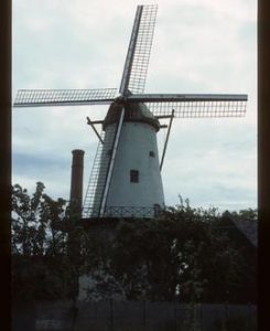Tall preserved tower mill with sails and stage; tall chimney adjacent