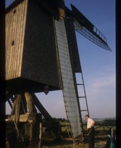 Man setting cloths on sails of restored open-trestle post mill