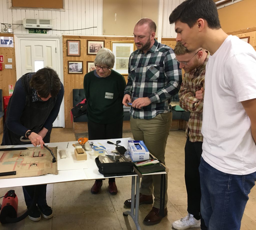 Group of volunteers watch a conservator working at the Mills Archive Trust